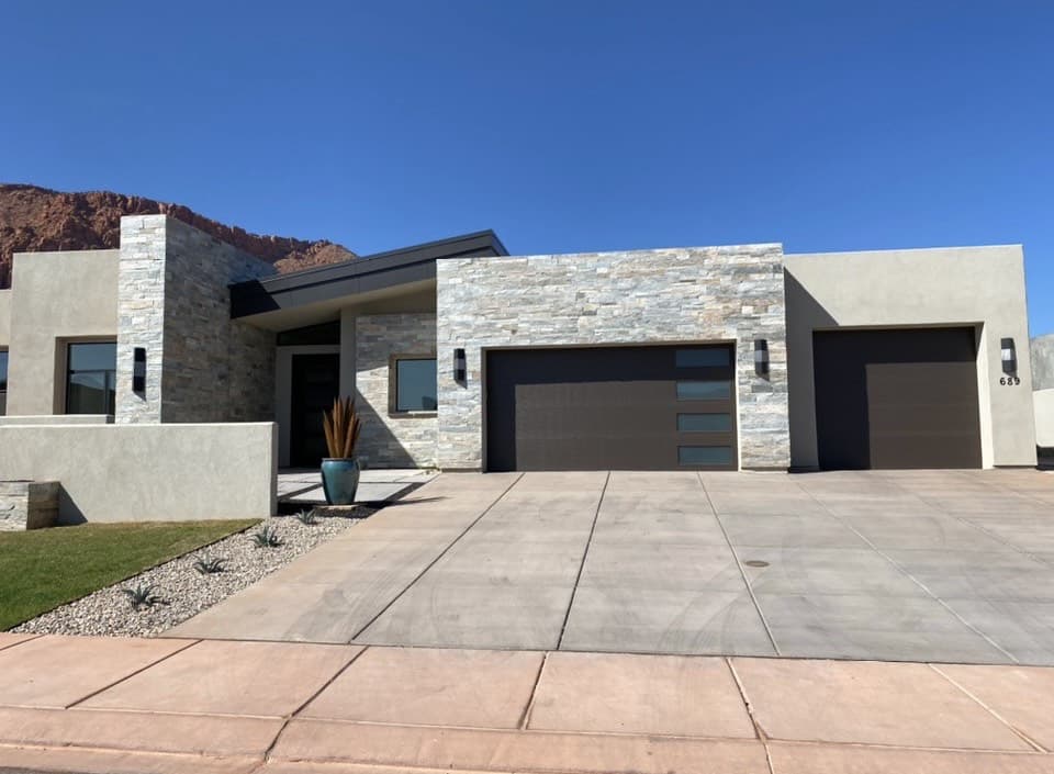 Single-level modern home with two-tone smooth stucco and light ledgestone at the entry tower and garage, red sandstone cliffs behind