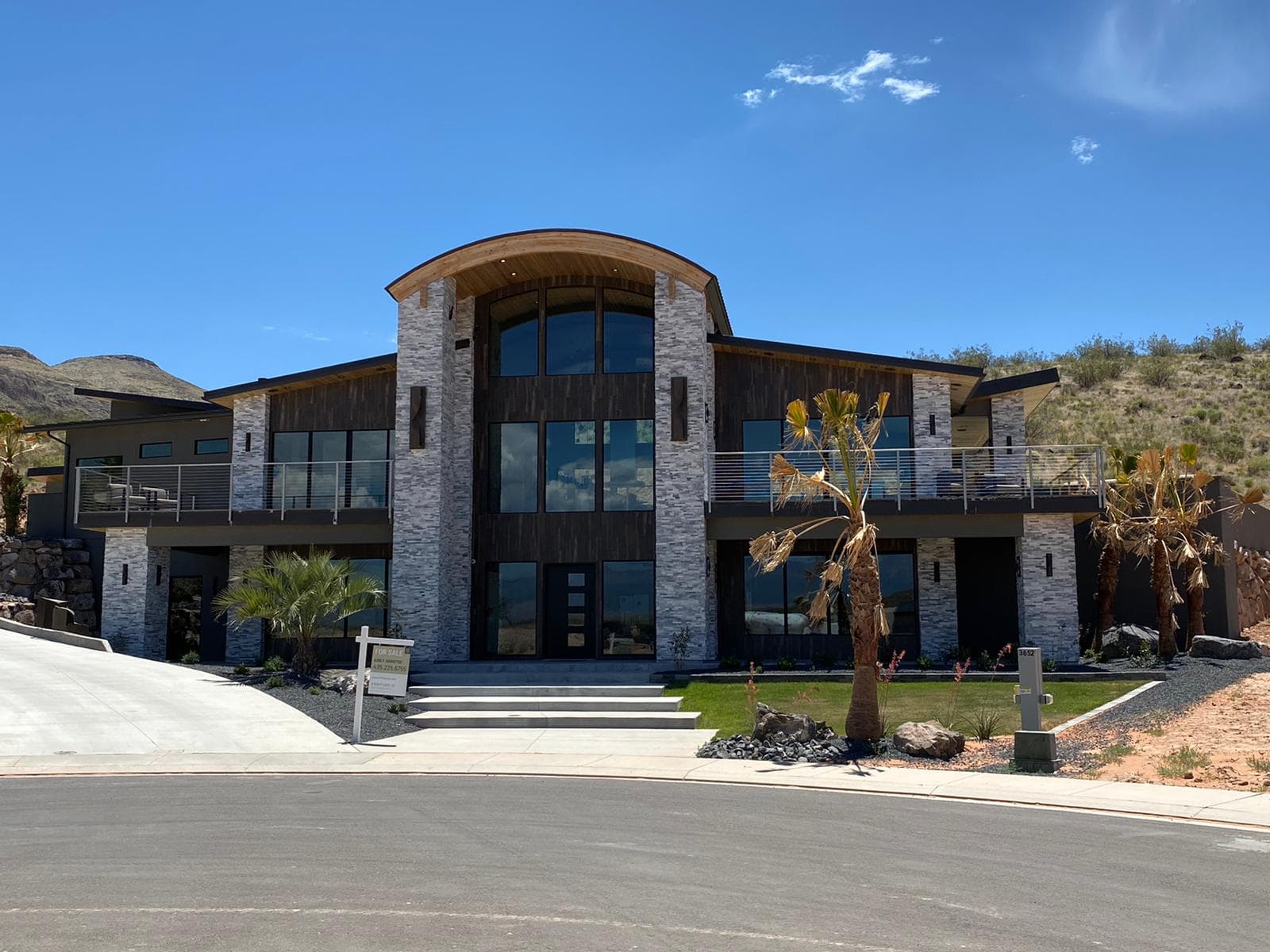 Two-story hillside home with full-height stacked stone towers around a glass entry, a curved wood soffit roof, and dark accent walls